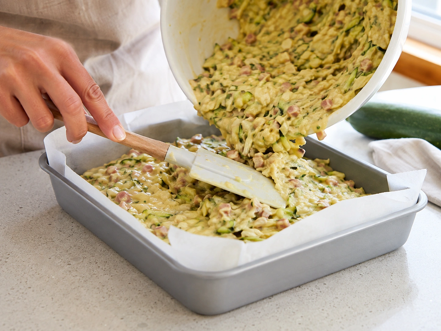 Pouring zucchini slice batter into a lined baking tin